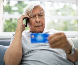 older man with unhappy face on the phone and looking at the back of a credit card