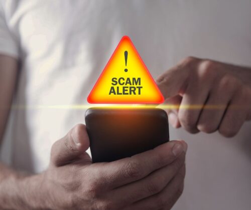 Man holding cell phone in his hand with a warning sign and "scam alert"