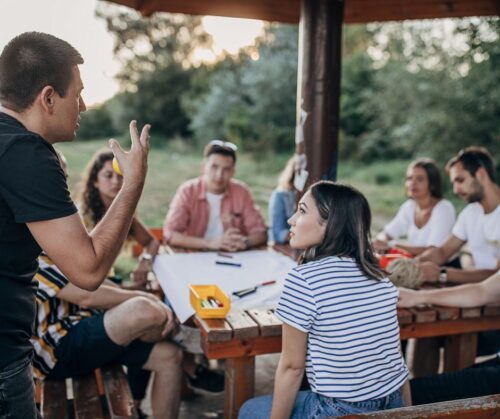 people outside, sitting around a table, having a meeting