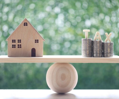 A toy house and stacks of coins on a seesaw