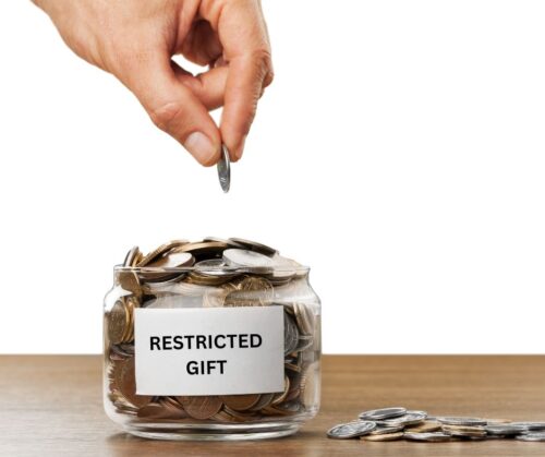 hand dropping coins into glass jar with a sign saying restricted gifts