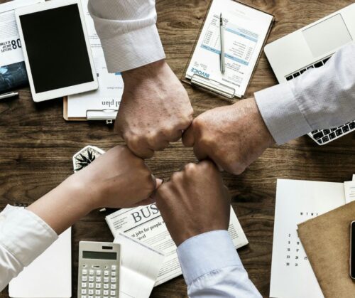 4 people bumping fists over a table of workpapers