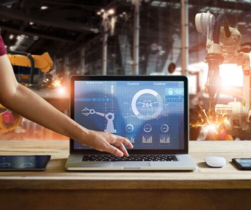 Man typing on computer to control machinery in the background.